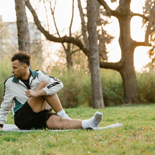 Smiling person stretching gently outdoors in a park at sunrise.